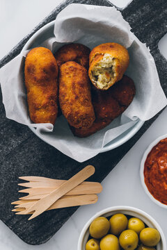 Top view of delicious fried broccoli croquettes in bowl served with various sauces and green olives