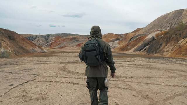 An unrecognizable person walks on dry cracked lifeless soil. A man in a protective suit on a background of a post-apocalyptic landscape. The concept of environmental pollution and global drought