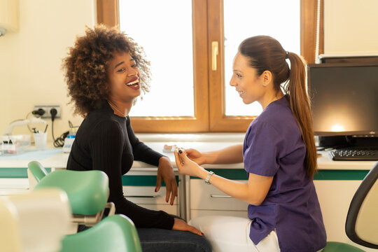 Cheerful African American lady talking with Caucasian female dentist about teeth implants in dental clinic