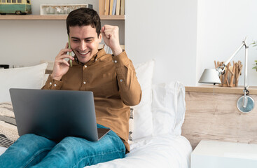 Hispanic man winner celebrate victory triumph using laptop and mobile phone at home - Focus on face