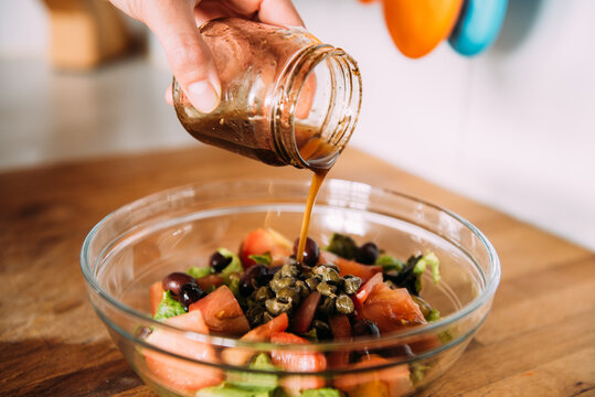 Crop anonymous housewife adding balsamic vinegar into bowl with fresh healthy vegetable salad while preparing lunch in kitchen