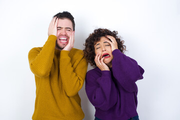 Young gloomy Young couple wearing knitted sweater standing against white wall, hiding face with...
