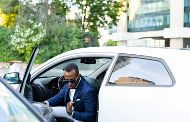 Serious African American male entrepreneur getting out of luxury automobile parked on road in city