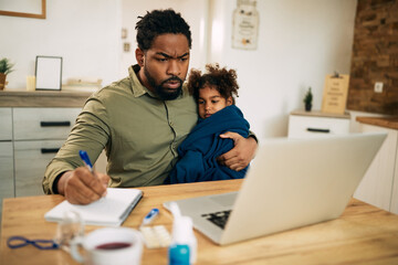 Obraz premium African American father working at home while holding his small daughter is feeling ill.