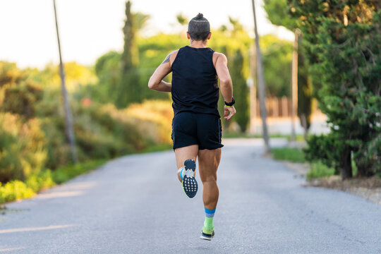 Back view of unrecognizable sportive male athlete in activewear running along path in park during cardio workout in summer
