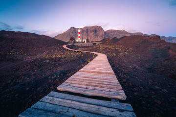 Winding pathway leading to beacon located on hill near sea on background of mountains in morning in Tenerife
