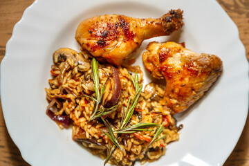 Marinated baked chicken drumsticks and wings with mushroom risotto in a plate on the table.