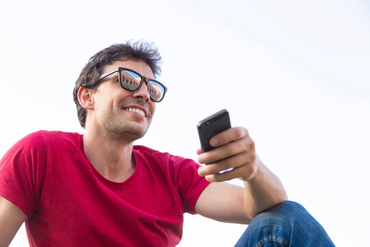 Attractive young man dressed with red t-shirt smiling with sunglasses and smartphone