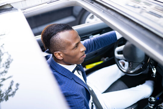 From below serious ethnic male entrepreneur in classy suit with bow tie driving luxury car looking away