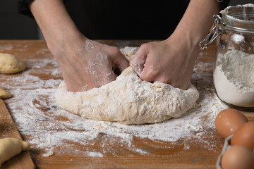 Young beautiful woman kneading dough at a wooden table in kitchen. Housewife hobbies concept.