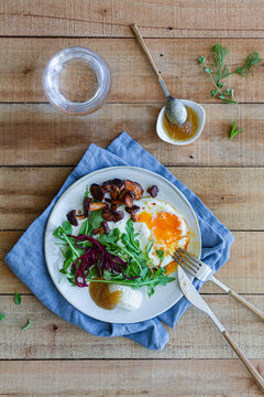 Top view of plate with palatable fried egg served with mushrooms and fresh salad on wooden table with sauce and glass of water