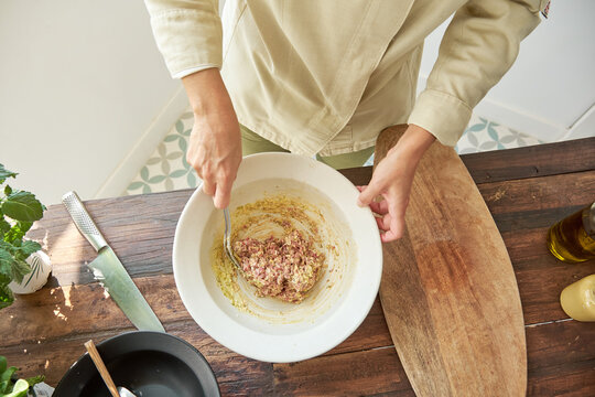 Top view of anonymous cook in uniform standing at table and mixing raw beef with mustard while preparing delicious Steak tartare