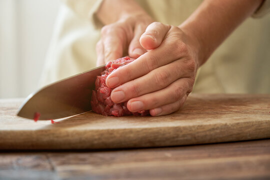 Unrecognizable crop housewife cutting fresh beef on wooden chopping board while preparing delicious Steak tartare for dinner at home