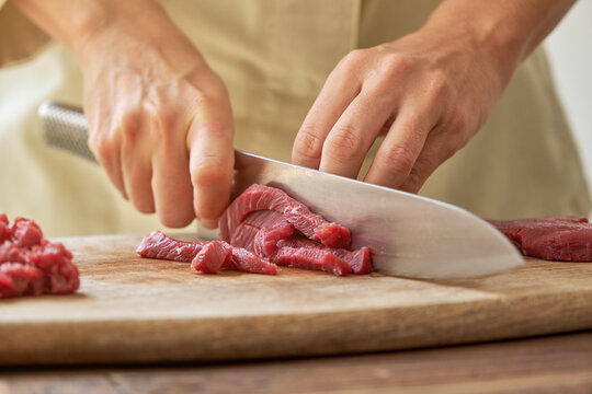 Unrecognizable crop housewife cutting fresh beef on wooden chopping board while preparing delicious Steak tartare for dinner at home