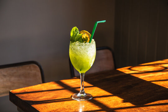 Glass of fresh appetizing icy cocktail with mint and lemon slice served with straw on wooden table in pub
