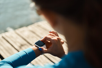 From above back view of unrecognizable female athlete sitting on mat and checking pulse on fitness tracker while resting after outdoor workout