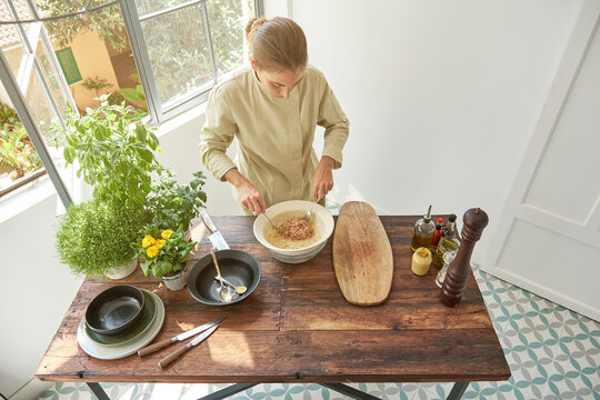 Top view of woman chef in uniform adding seasonings with pepper mill in bowl with raw beef and mustard while cooking appetizing Steak tartare at home