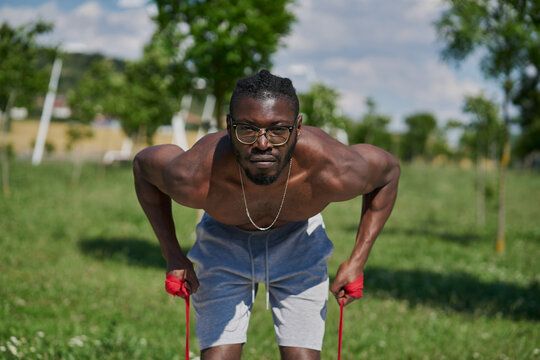 Strong Active African American Male With Naked Muscular Torso Doing Resistance Bend Bicep Curl Exercise During Functional Workout On Street