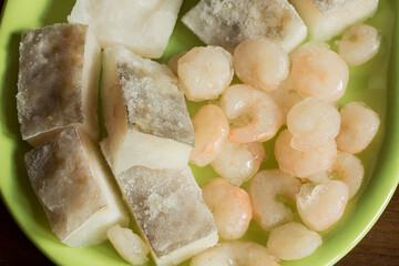 A green plate with delicious cod loins and prawns with ice remnants. Frozen food.