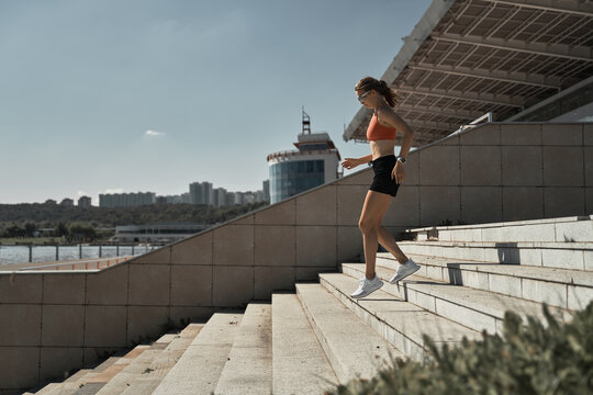 Side view of energetic determined female athlete in sportswear running downstairs on tribune of stadium during outdoor fitness training