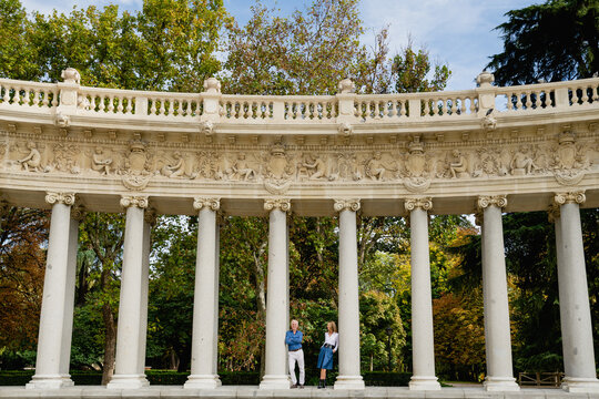 Remote view of couple leaning on stone columns of arched passage in urban park during summer stroll