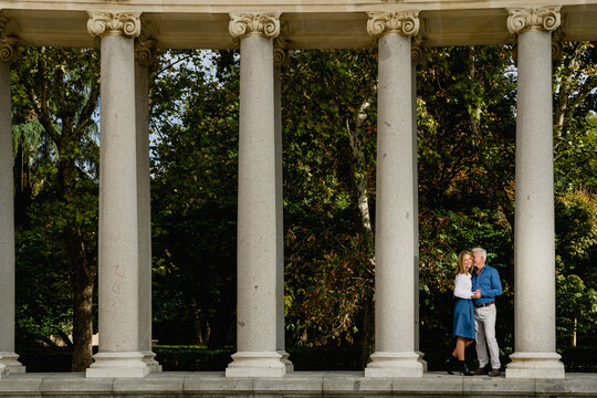Remote view of couple leaning on stone columns of arched passage in urban park during summer stroll