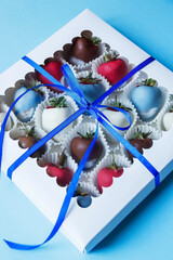 Chocolate covered strawberries in a gift box on a blue background, dessert for Valentine's Day, romance, food as a gift. Homemade chocolate covered strawberries. Romantic postcard with free space.