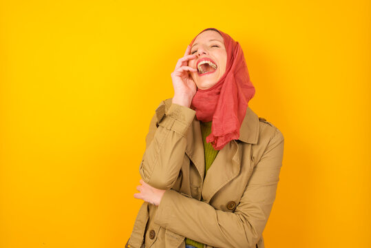 Charismatic Carefree Joyful Young Caucasian Muslim Woman Wearing Hijab Standing Against Yellow Wall Likes Laugh Out Loud Not Hiding Emotions Giggling Hear Funny Hilarious Joke Chuckling Facepalm.