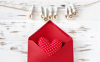 Valentines day. Red envelop and heart shape on white wooden background, inscription from wooden letters.