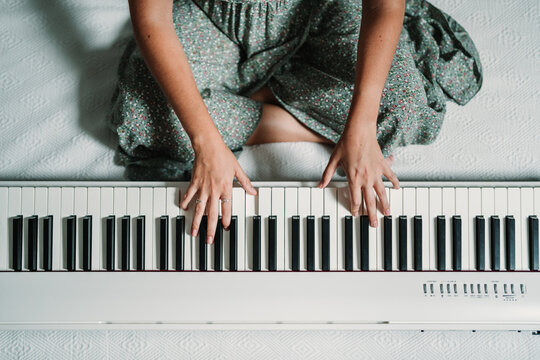 From above of talented ethnic female musician playing piano while sitting in modern apartment and rehearsing