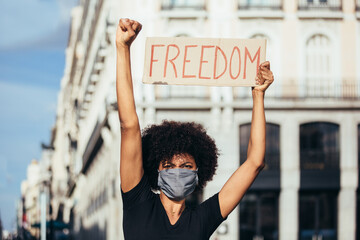 Afro woman protesting at a rally for racial equality. She is raising fist holding a sign with the word "Freedom". Black Lives Matter.