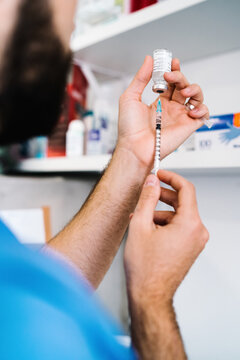Unrecognizable crop male doctor filling syringe with liquid medication while standing in bright medical room in clinic