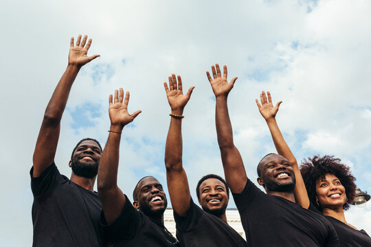 Cheerful black men and woman raising hands against a blue sky
