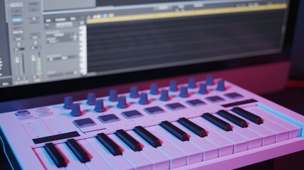 Male hands recording music, playing electronic keyboard, midi keys on the table with neon lights....