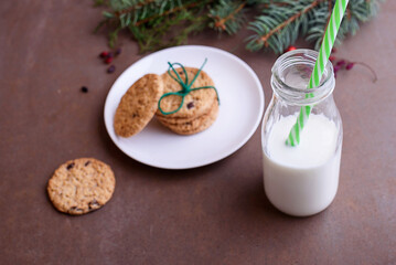 Shortbread cookies with pieces of chocolate on a white plate, tied with a thread. Milk in a glass bottle. View from above. Tree twigs.