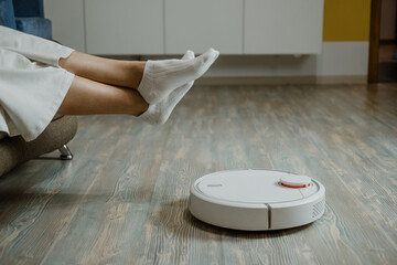 Robotic Vacuums, Robot Mops. Smart home. Robotic Vacuum Cleaner while Woman Relaxing on sofa....