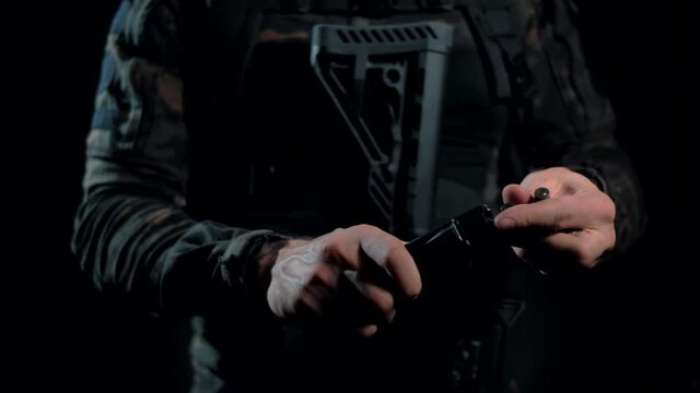 Military man inserts cartridges into a rifle magazine. Close-up. Black background