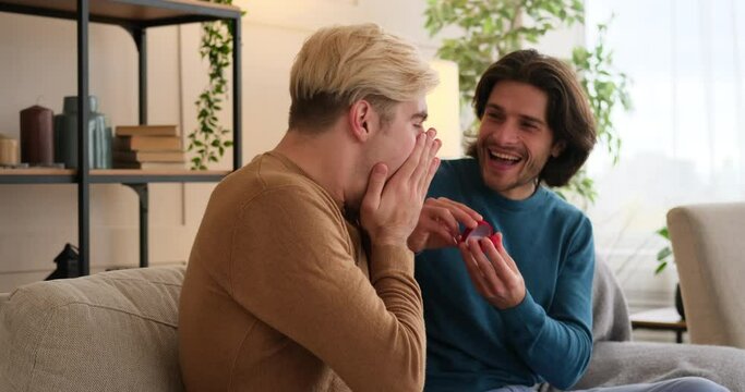 Gay man proposing boyfriend with an engagement ring in red box at home