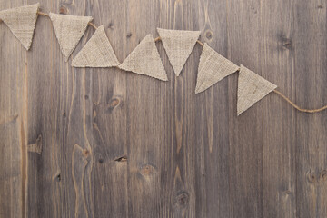 Triangle linen party flags on wooden background. Small sackcloth bunting garland on wood planks...