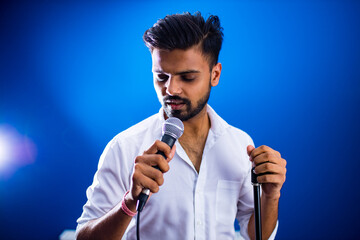 indian man in white shirt with beard singing in recording studio on blue background