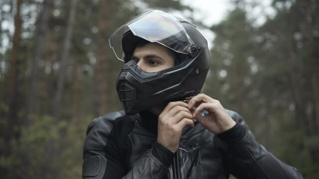 Portrait of handsome Middle Eastern man putting on motorcycle helmet and leather biker gloves. Confident serious male motorcyclist sitting on motorbike. Racing and lifestyle concept.