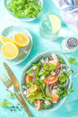 Bowl of healthy vegetable salad with various leaf salad, tomatoes, feta cheese, onions, olive oil, light blue concrete background copy space