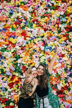 Cheerful female friends embracing while standing against colorful flowers