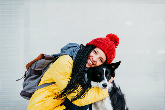 Happy woman embracing pet dog against wall