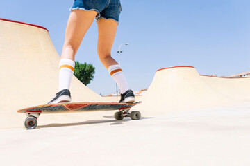 Legs of young woman skateboarding on sports ramp against clear blue sky at park