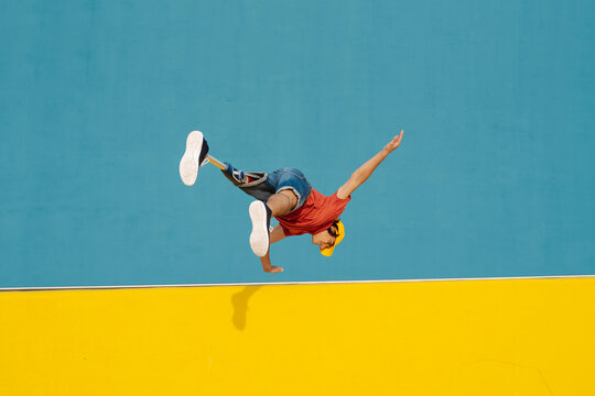 Athlete practicing handstand while jumping against multi colored wall