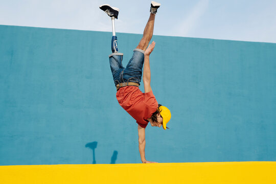 Young man with artificial limb and foot doing handstand against multi colored wall