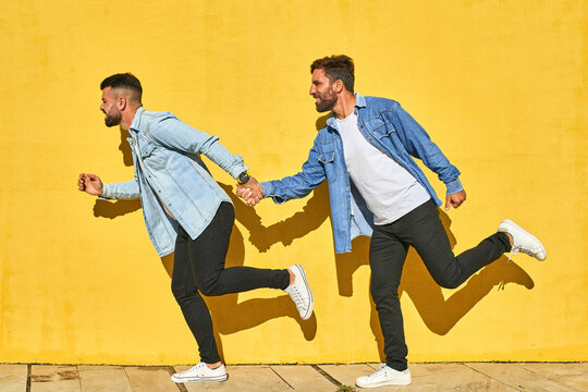 Gay couple holding hands while running against yellow wall