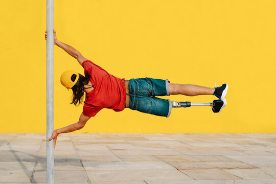 Young athlete holding pole while balancing body weight against multi colored wall