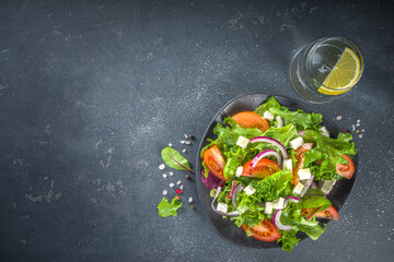 Bowl of healthy vegetable salad with various leaf salad, tomatoes, feta cheese, onions, olive oil, dark grey concrete background copy space